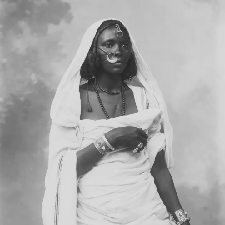 Retrato de una mujer africana vestida con trajes tradicionales y joyas decorativas.